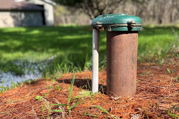 Residential well cap and casing in a yard, typical of a private well on a rural property